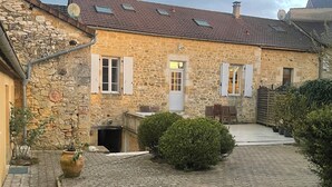 A stone building with a tiled roof, a door, and a small courtyard with potted plants. - Charming house in the heart of the Lot (Gourdon)