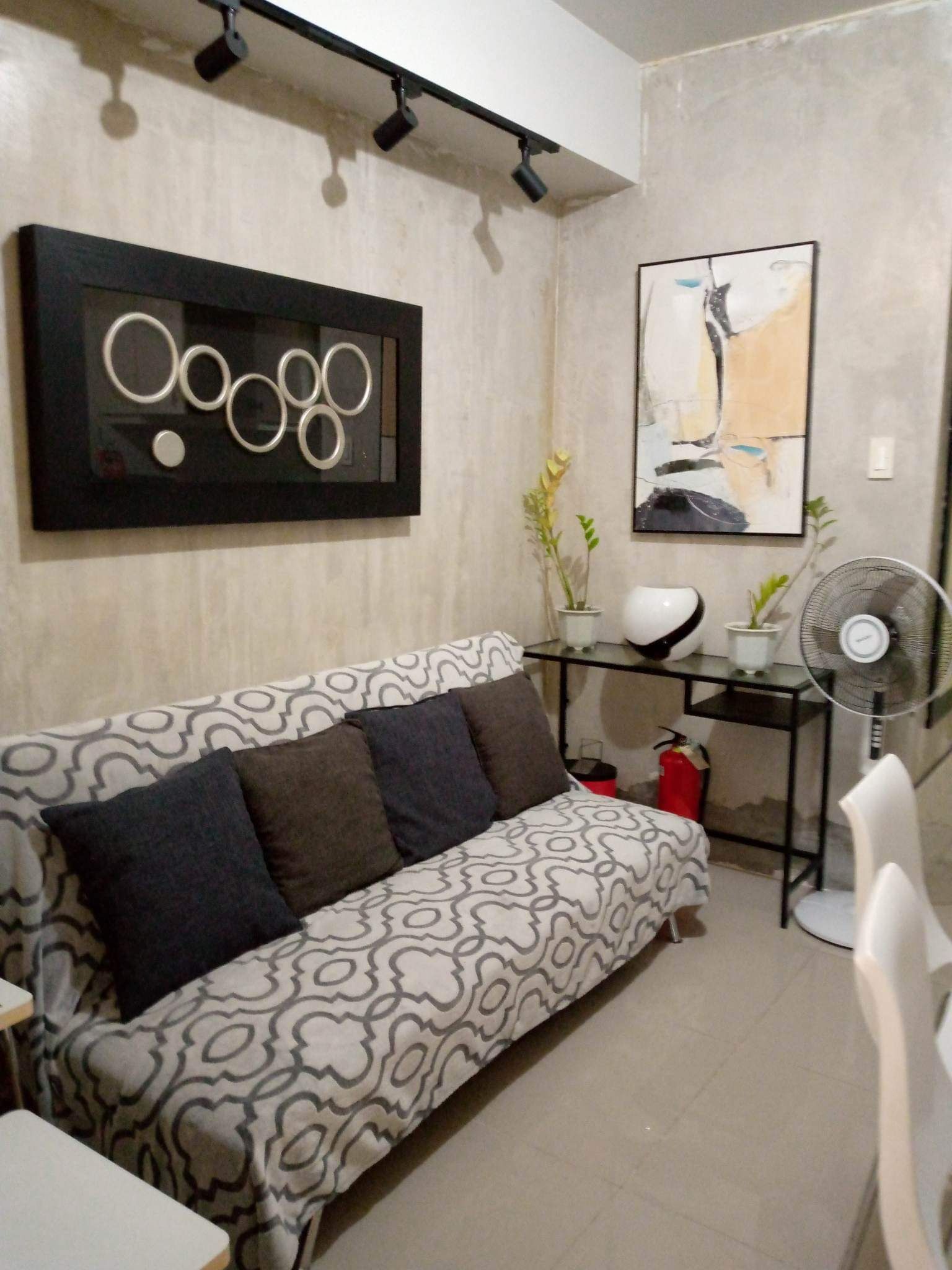 Una sala moderna con un sofá estampado, una mesa de centro, un cuadro abstracto colgado en la pared, una lámpara de pie y un ventilador de pie.
