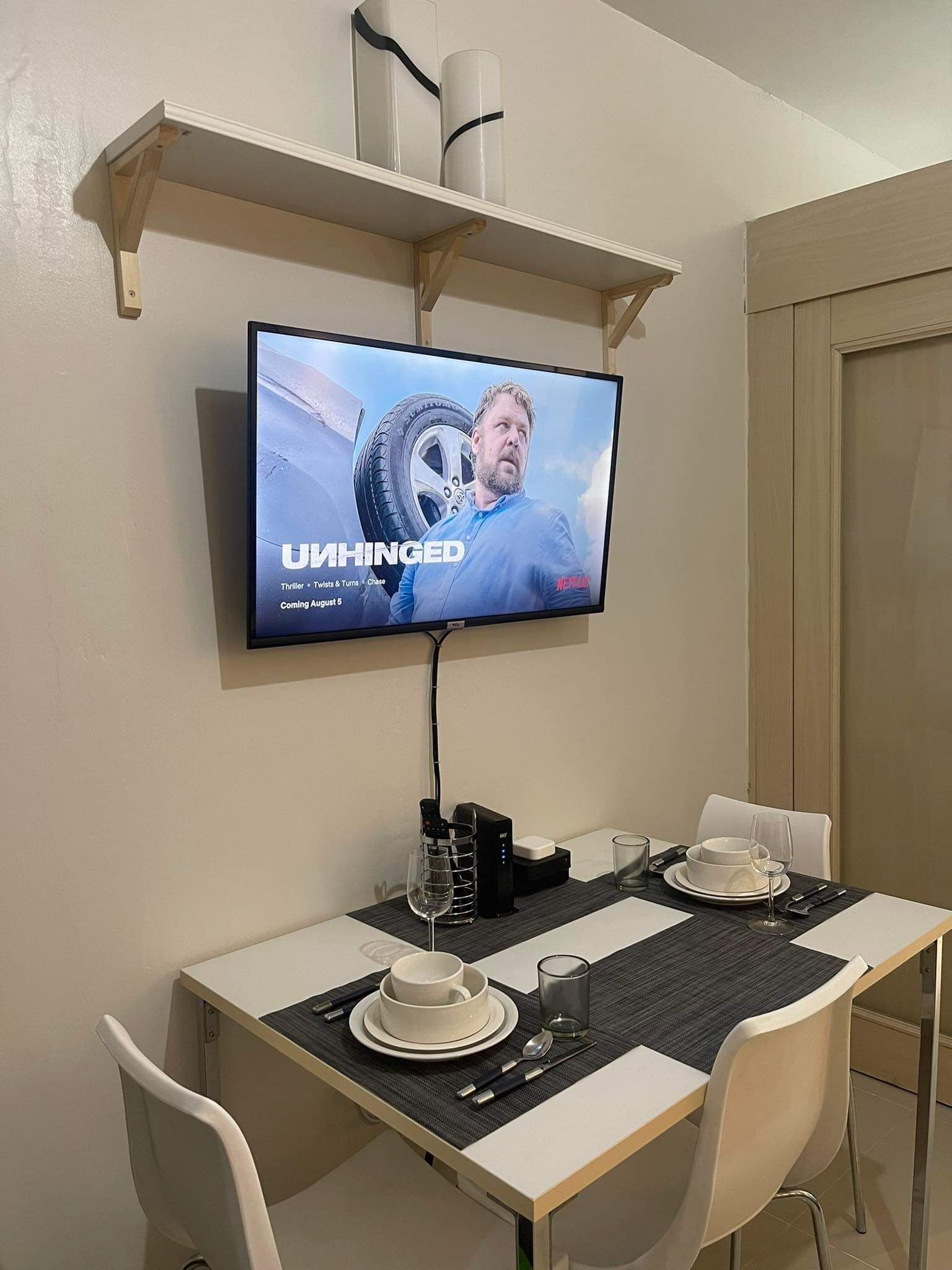 A dining area with a TV displaying 'UHINGED' on the screen, a table set with plates, glasses, and cutlery, and a chair.