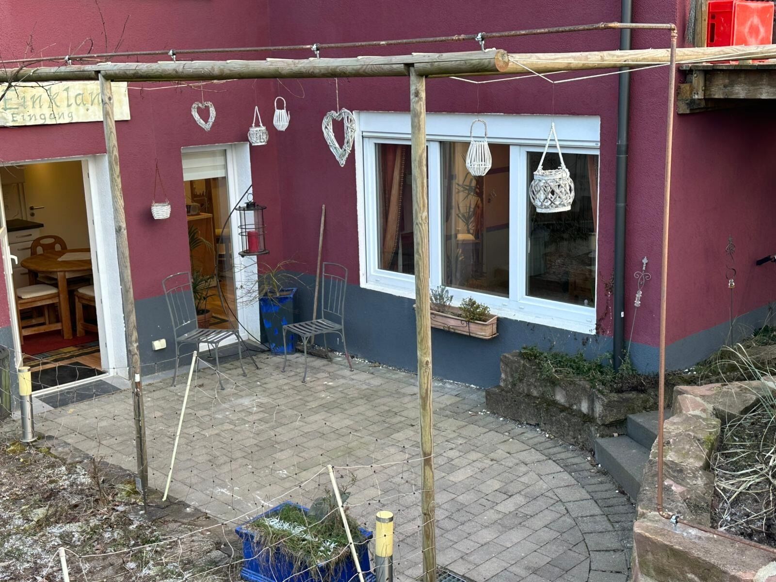 Ein Gebäude mit einer Holzpergola, einem Schild mit der Aufschrift 'Einklang Eingang' und einem Fenster mit einer hängenden Laterne.