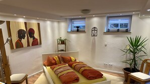Een moderne slaapkamer met een groot bed, twee ramen, een kamerplant en kunstwerken aan de muren.