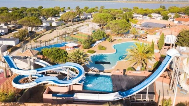 En vandpark med flere rutsjebaner og en swimmingpool, omgivet af grøn bevoksning og bygninger.