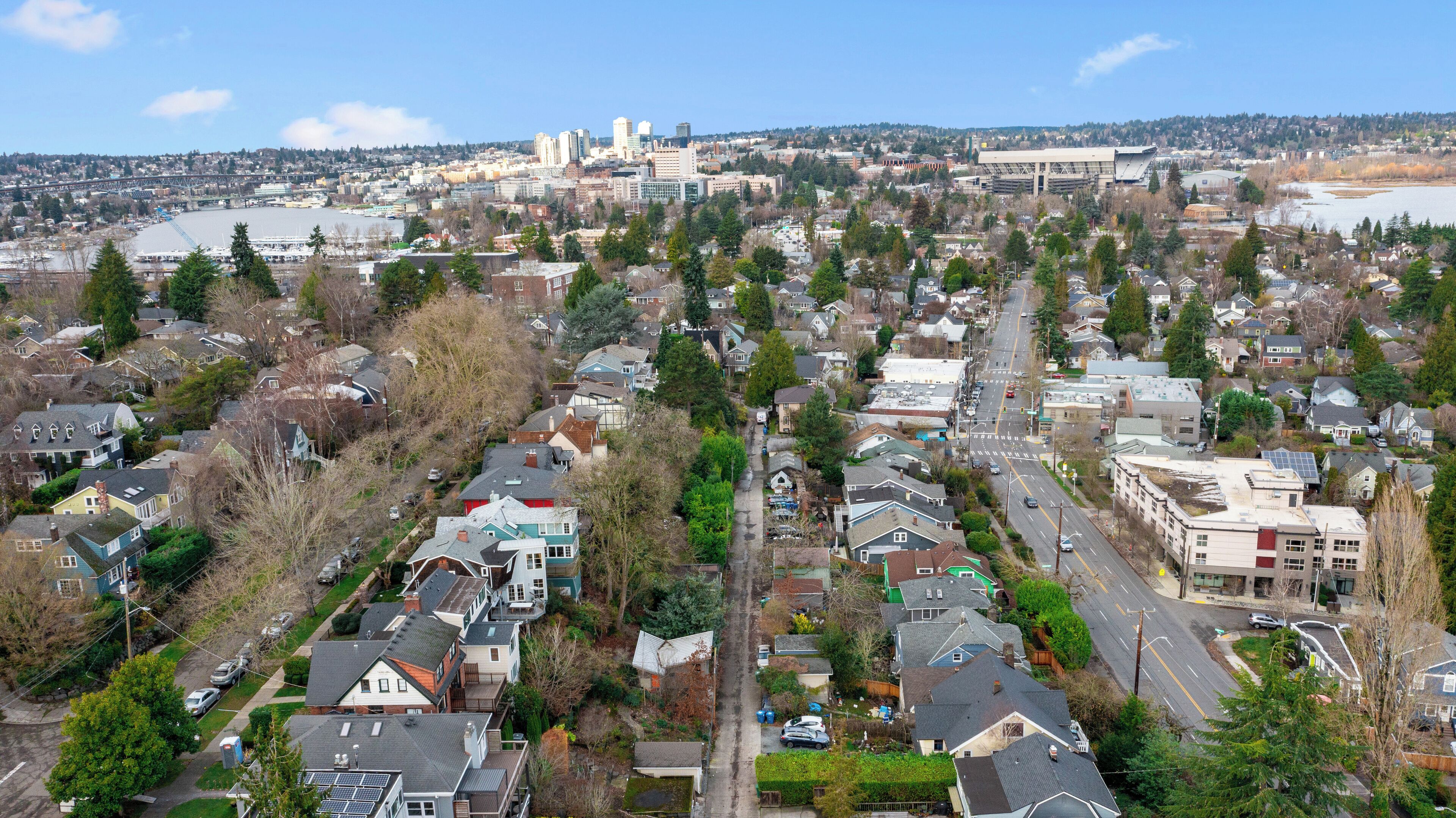A residential area with houses, streets, and a distant view of a city skyline including a bridge and a stadium.