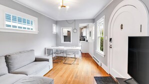 A modern living room with a grey sofa, a dining table with chairs, a TV, and a kitchen area visible through an open door. - Montlake Hideaway in Spite House (Seattle)