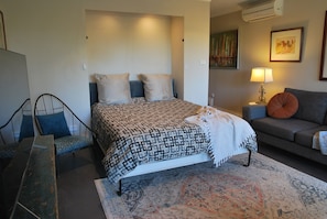 Un dormitorio con cama, sofá, sillón, lámpara y un cuadro en la pared.