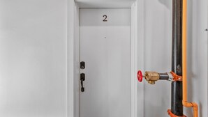 Una puerta blanca con el número 2, un pomo negro y un botón de parada de emergencia rojo.