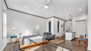 Un dormitorio moderno con cama, una silla, escritorio y kitchenette.