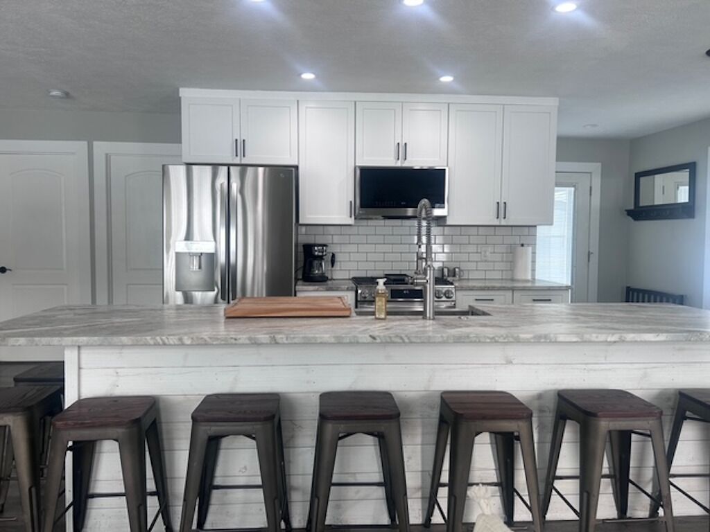 Una cocina moderna con armarios blancos, un refrigerador de acero inoxidable, horno empotrado y una isla grande con taburetes de bar.
