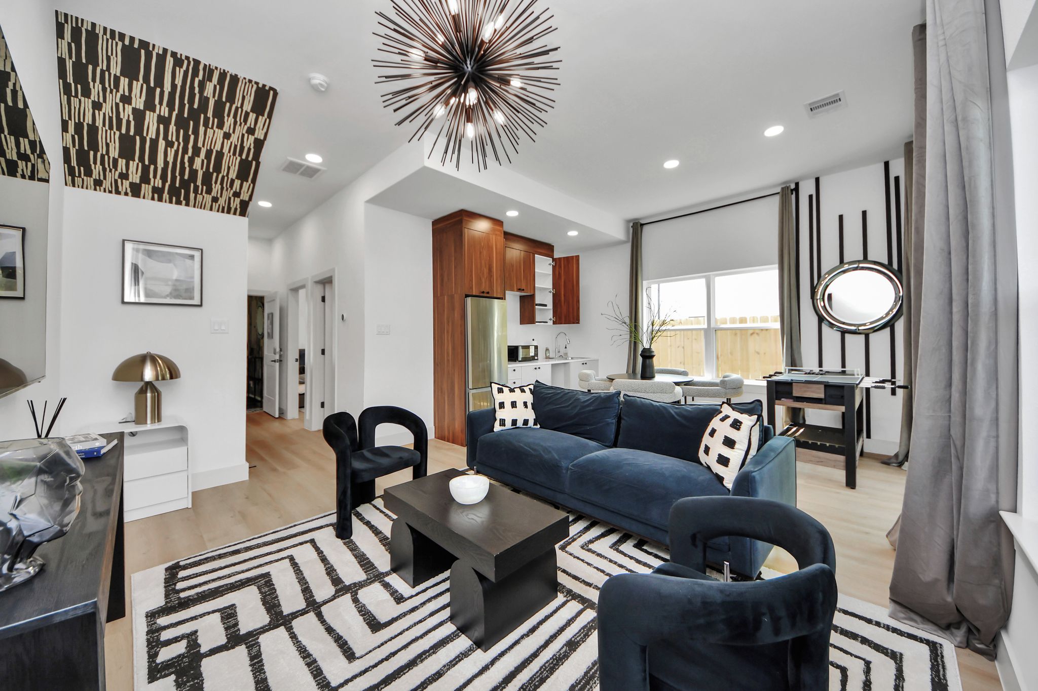A modern living room with a sofa, chairs, a coffee table, and a kitchen area in the background.