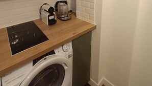 Eine kompakte Küche mit Waschmaschine, Kaffeemaschine und einem gerahmten Bild von Paris an der Wand.
