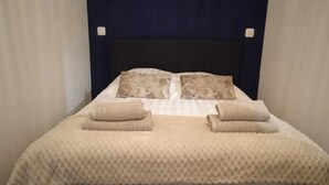 Ein ordentlich bezogenes Bett mit einer beigefarbenen, strukturierten Tagesdecke, zwei Kissen mit Blumenmuster und zwei aufgerollte Handtücher.