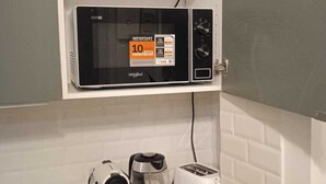 Eine Küche mit Mikrowelle, Kaffeemaschine, Toaster sowie einem Regal mit Weingläsern und Schüsseln.