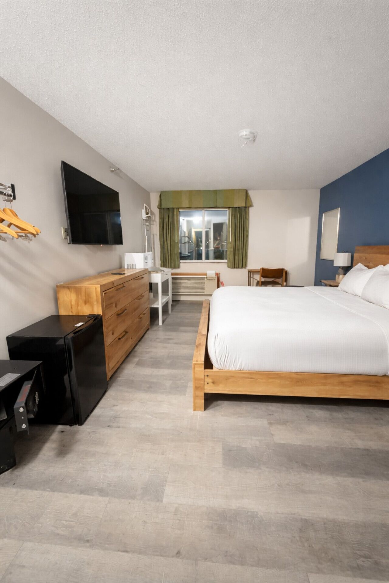 Moderni hotellihuone, jossa on puinen sänky, litteänäyttöinen televisio, puinen lipasto ja pieni pöytä.