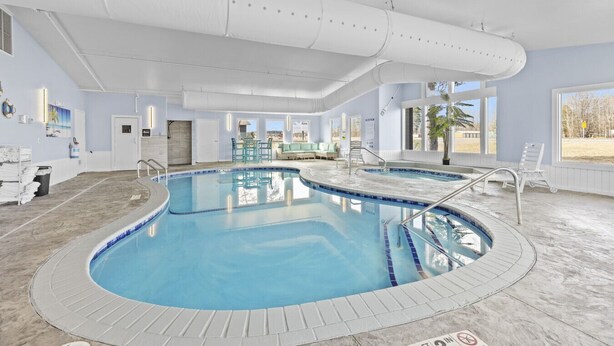 Una piscina interior con borde de azulejos, un área de descanso con sillones y vistas al exterior.