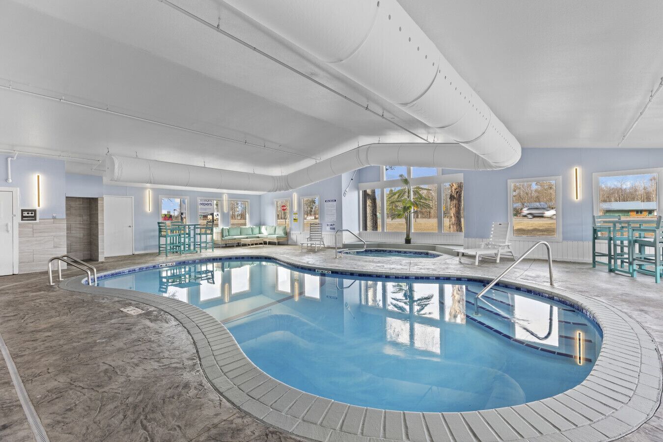 Une piscine intérieure dotée d’une terrasse carrelée, de chaises longues et offrant une vue sur l’extérieur.