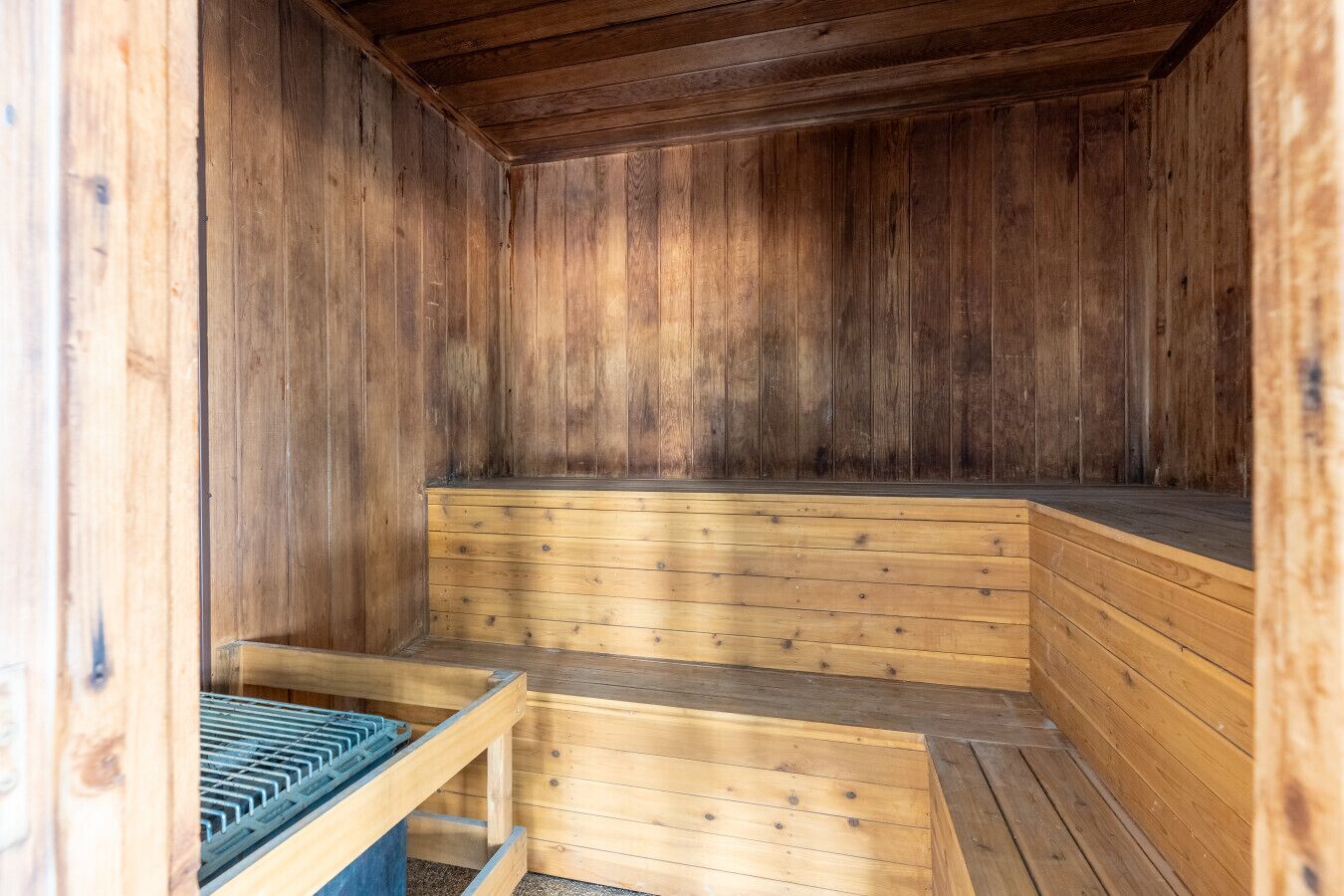 Un sauna avec des bancs en bois et un banc doté d’une grille métallique.