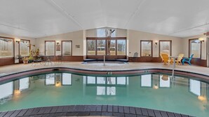 An indoor swimming pool with clear water, surrounded by a lounge area with chairs and tables, large windows, and a view of the outdoors. - King Room Retreat in Nisswa – Indoor Pool, Sauna & Near Gull Lake (Nisswa)