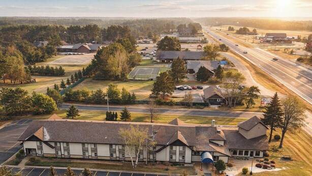 An aerial view of a small town with a prominent building with a large garage door, surrounded by trees and a road. - King Room Retreat in Nisswa – Indoor Pool, Sauna & Near Gull Lake (Nisswa)