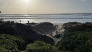 Ein Strand mit blauem Himmel, Wellen und einer Person, die im Sand steht.