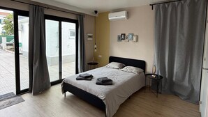 Ein modernes Schlafzimmer mit einem großen Bett, einem Deckenventilator, einer Klimaanlage und Blick durch die Glastür.