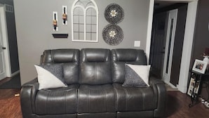 A black leather sofa with two pillows, a white-framed window, and decorative wall art. - 3-bedroom home with great  backyard  & pool with a  private and peacful setting (Spring Hill)
