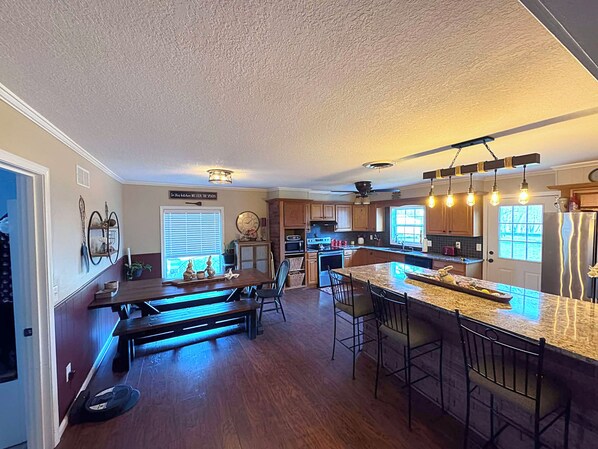 A kitchen with a central island, bar stools, wooden flooring, and pendant lighting.