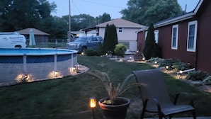 A backyard with a swimming pool, a lawn, a patio with a chair and a table, and a house in the background. - 3-bedroom home with great  backyard  & pool with a  private and peacful setting (Spring Hill)