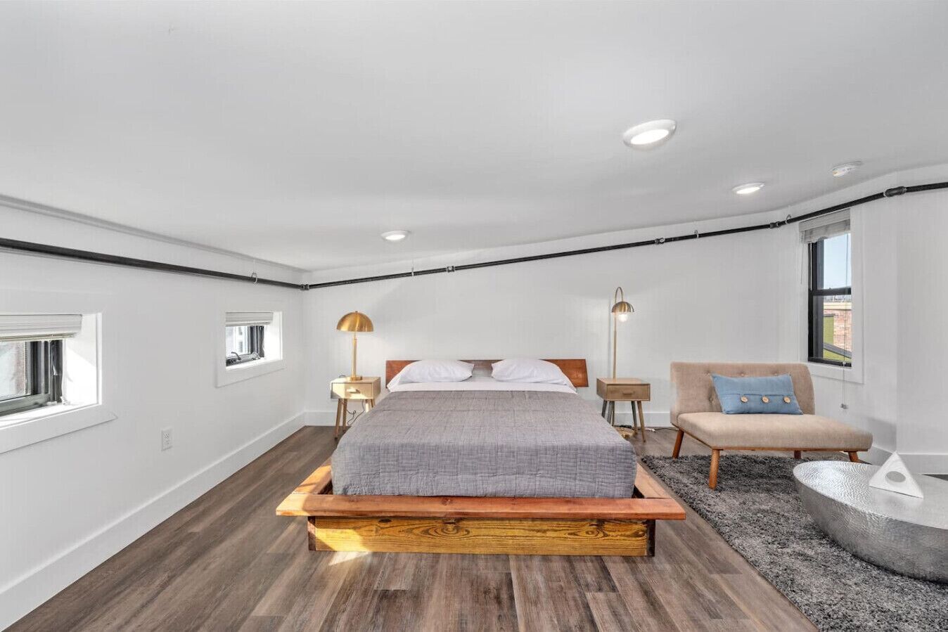 Un dormitorio moderno con una cama plataforma de madera, un pequeño rincón de descanso y una mesa redonda.