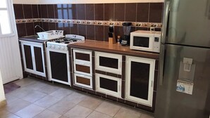 A compact kitchen with a gas stove, microwave, refrigerator, and white cabinets with black doors. - 22 - Casa en Acapulco Zona Diamante Joyas del Marques - Alojamiento entero (Acapulco)