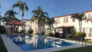 A swimming pool surrounded by palm trees and a building with a red-tiled roof. - 22 - Casa en Acapulco Zona Diamante Joyas del Marques - Alojamiento entero (Acapulco)