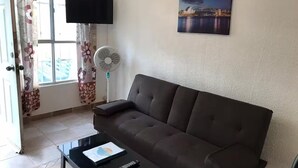 A living room with a brown sofa, a black coffee table with a remote control, a flat-screen TV, and a cityscape painting on the wall. - 22 - Casa en Acapulco Zona Diamante Joyas del Marques - Alojamiento entero (Acapulco)
