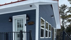 A house with a dark blue exterior, a white door, and a 'Welcome Friends' sign. - Lakeside cottage with lake and mountain views, boat launch access & amenities. (Westport)