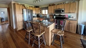 A kitchen with wooden cabinets, a central island with stools, a microwave, and a refrigerator. - Lakeside cottage with lake and mountain views, boat launch access & amenities. (Westport)