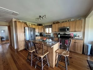 A kitchen with wooden cabinets, a central island with stools, a microwave, and a refrigerator.