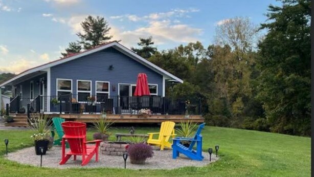 A house with a covered porch, outdoor seating with colorful Adirondack chairs, and a well-maintained lawn. - Lakeside cottage with lake and mountain views, boat launch access & amenities. (Westport)