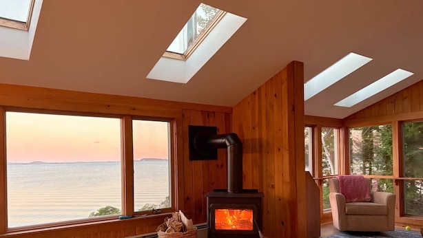 A cozy room with a wood-burning stove, large windows, and a view of the water. - Barnacle - quiet family Maine waterfront getaway (Harpswell)