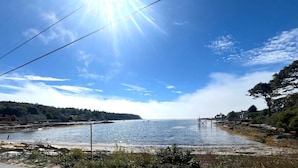 A coastal view with a pier extending into calm waters, surrounded by greenery and a clear sky. - Barnacle - quiet family Maine waterfront getaway (Harpswell)
