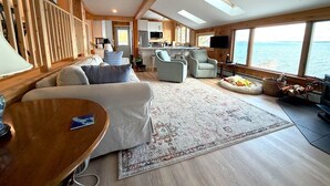 A spacious cabin with a large window offering a view of the sea, a cozy seating area with a sofa and armchairs, a small kitchen, and a flat-screen TV mounted on the wall. - Barnacle - quiet family Maine waterfront getaway (Harpswell)