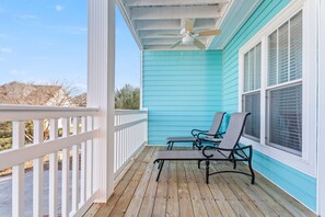 A covered porch with two chairs, a ceiling fan, and a view of the outside.