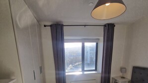 A bedroom with a bed, a dresser, a window with curtains, and a lamp.