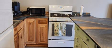 A kitchen with wooden cabinets, a white refrigerator, a microwave, a stove, and hanging light bulbs.