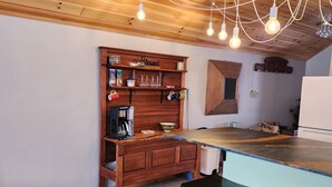 A kitchen with wooden ceiling, a wooden shelf with various items, a coffee maker, and a bar counter with stools. - Lakeside oasis Apt with water access and views.
There is a She shed on the beach (Norwood)