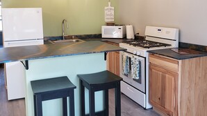 A modern kitchen with a wooden ceiling, a built-in stove, a microwave, and a sink. There are two black stools and a sign that reads "Kitchens Together". - Lakeside oasis Apt with water access and views.
There is a She shed on the beach (Norwood)