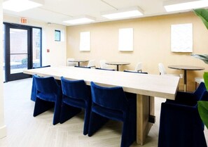 Une salle de conférence avec une longue table et des chaises bleues, une porte avec un panneau indiquant la sortie, et des tableaux encadrés accrochés au mur.