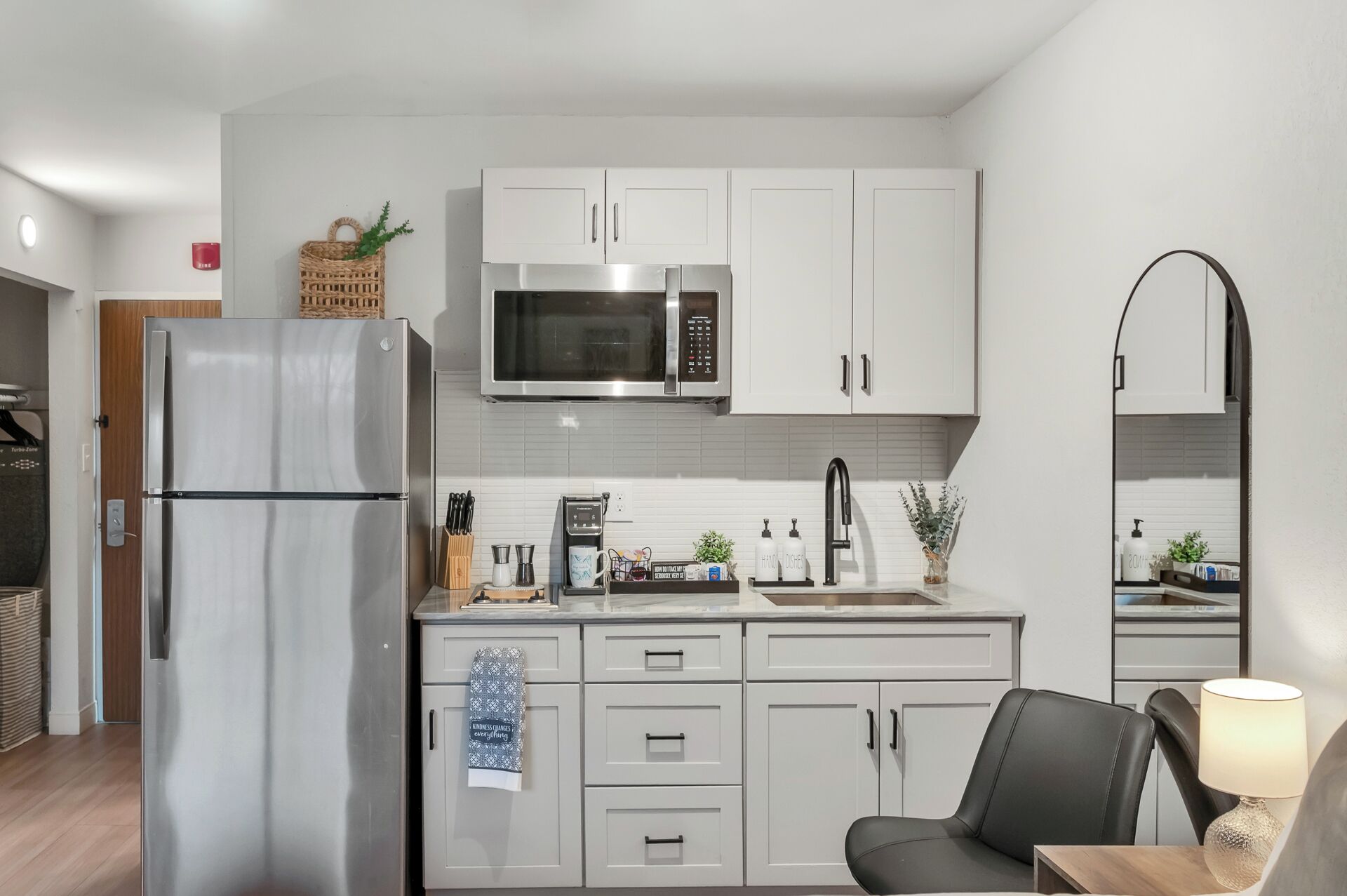 A modern kitchen with white cabinets, stainless steel appliances, and a black chair.