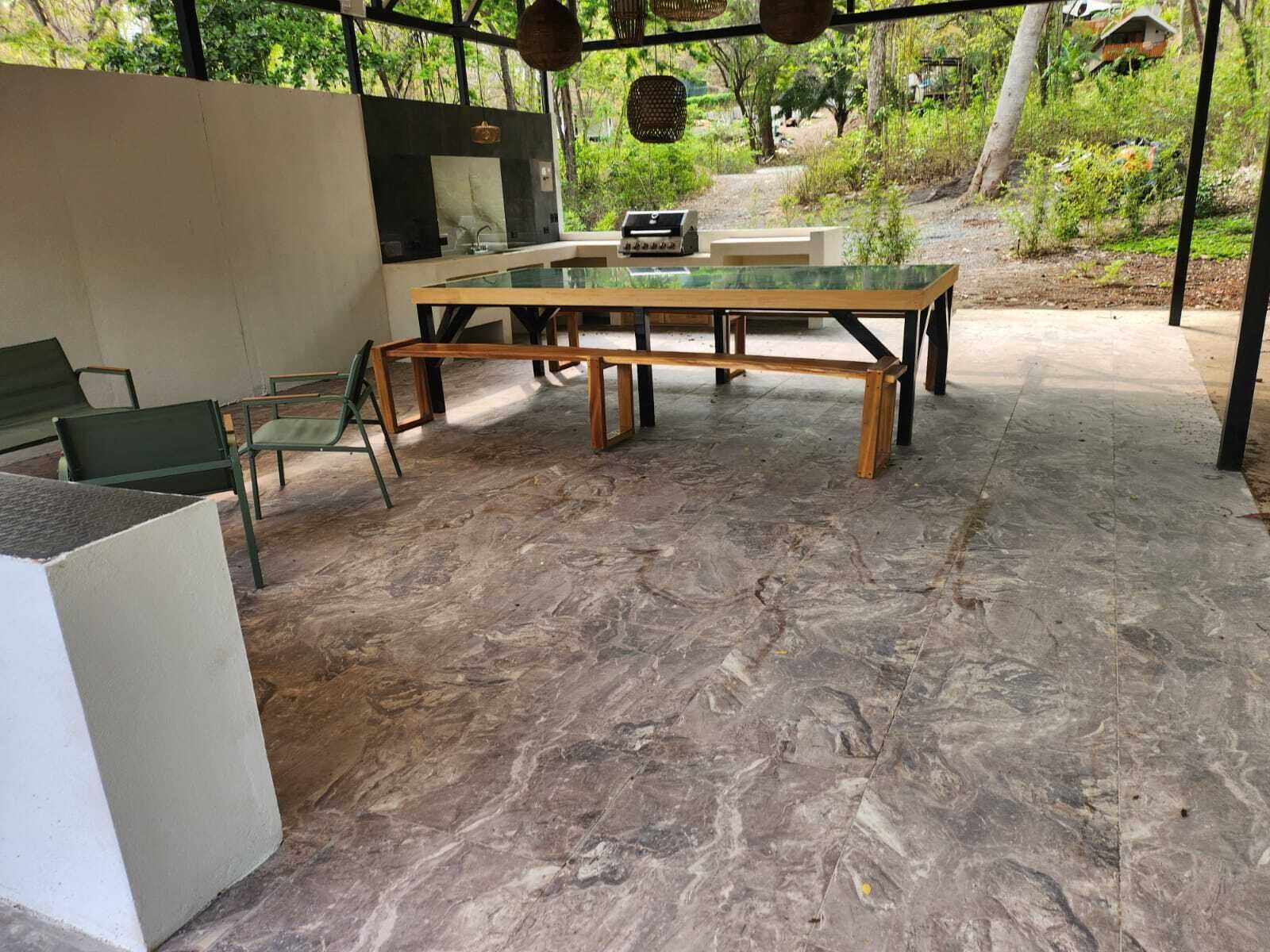 Une terrasse extérieure avec une table à plateau en verre, des chaises vertes et un sol en pierre.