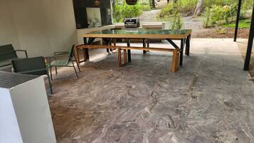 Une terrasse extérieure avec une table à plateau en verre, des chaises vertes et un sol en pierre.