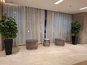 Eine moderne Lobby mit großen Fenstern, zwei grauen Hocker und Topfpflanzen.