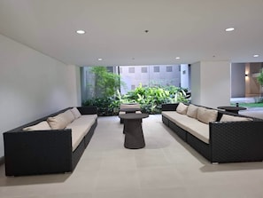 Ein moderner Außenbereich zum Sitzen mit zwei Sofas und einem Couchtisch, umgeben von üppigem Grün und Blick auf ein Gebäude im Hintergrund.