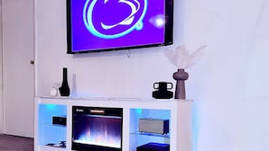 A modern living room with a flat-screen TV mounted on the wall, a fireplace, and a white entertainment unit with a vase and a small table.